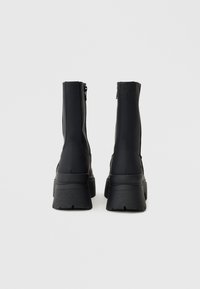 Melni potīšu zābaciņi ar augstu, strukturētu platformu, gludu gumijas virsu un rāvējslēdzēju aizmugurē.