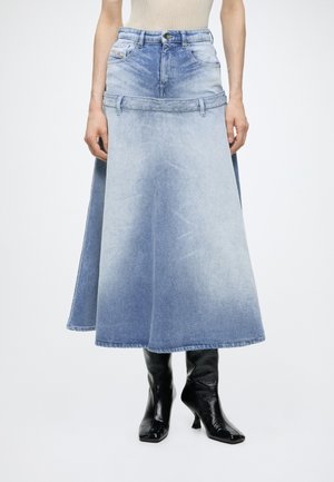 Gonna di jeans azzurro chiaro con taglio ampio a trapezio e una cintura che somiglia a quella dei jeans, indossata con stivali neri con tacco.