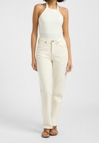 Bodysuit halter côtelé blanc associé à un jean taille haute beige clair. Présente un design ajusté et une jambe droite avec un style classique à cinq poches.