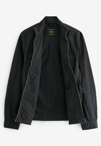 Veste noire légère avec fermeture éclair, col montant et deux poches latérales ; tissu texturé et étiquette intérieure visible.