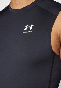 Marineblå ermeløs treningstrøye laget av elastisk stoff, med en hvit Under Armour-logo på brystet og synlige sømdetaljer.