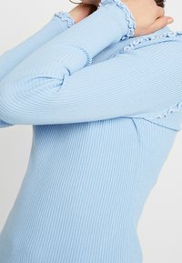 Hellblau gestreiftes Langarmoberteil mit Rüschenakzenten am Kragen und den Ärmel, einer figurbetonten Silhouette und strukturiertem Stoff.