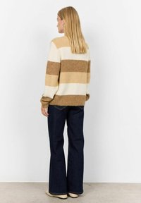 Hnědo-beige pruhovaný pletený svetr, volný střih, s dlouhými rukávy, spojený s tmavě modrými zvonovými džíny a béžovými botami.