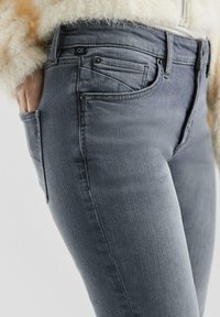 Schlanke graue Jeans aus Denim. Verfügt über Fronttaschen und sichtbare Nähte. Der Stoff hat eine glatte Textur mit leichter Abnutzung.
