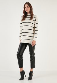 Maglione beige a righe con linee orizzontali nere, abbinato a pantaloni in pelle neri aderenti e stivaletti con fibbia.