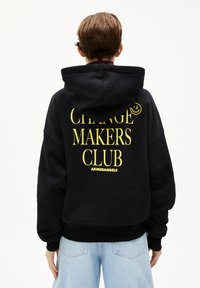 Zwarte hoodie met grote gele tekst: "CHANGE MAKERS CLUB" en logo, met een ontspannen pasvorm en een trekkoord in de capuchon.