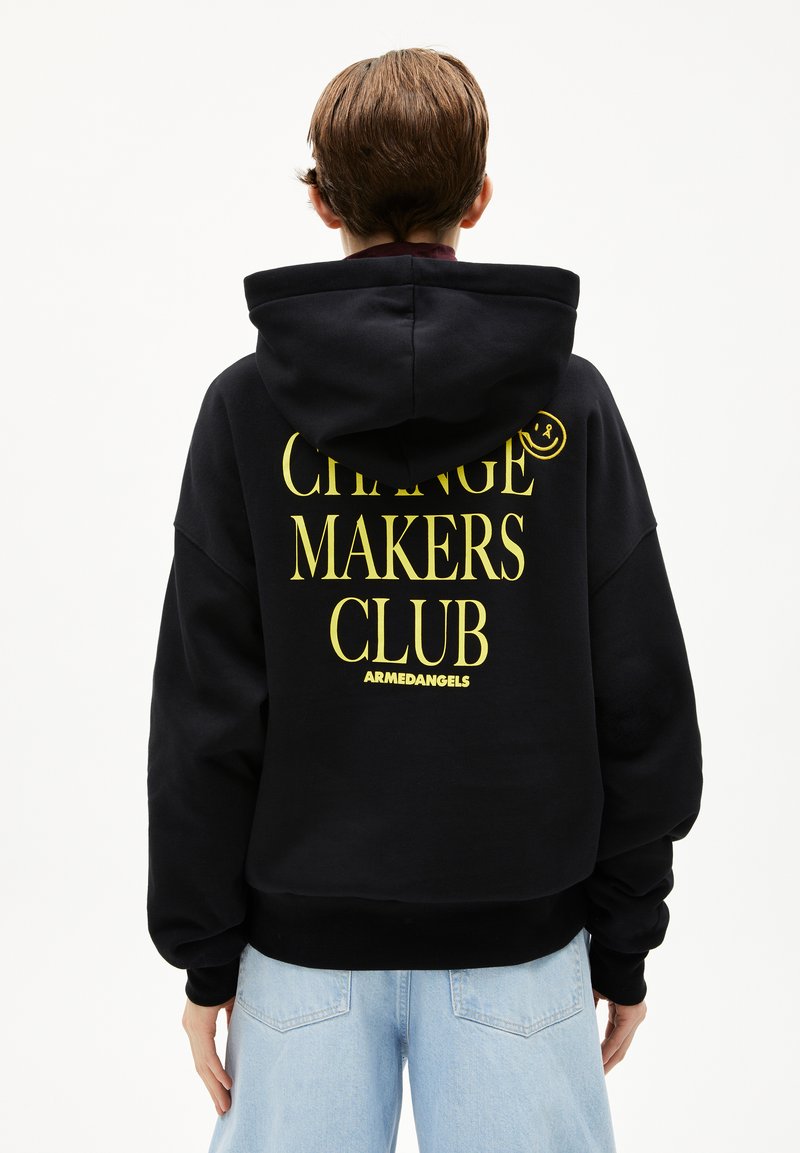 Zwarte hoodie met grote gele tekst: "CHANGE MAKERS CLUB" en logo, met een ontspannen pasvorm en een trekkoord in de capuchon.