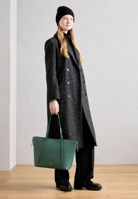 Sort tekstureret dobbeltradet frakke, sort rullekrave, grøn lædertaske med lange stropper, sorte bukser og chunky sorte sko.