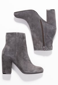Bottines en suede gris à bout pointu, avec un talon épais et un détail de fermeture éclair sur le côté. Présentent une texture lisse et un design moderne et épuré.