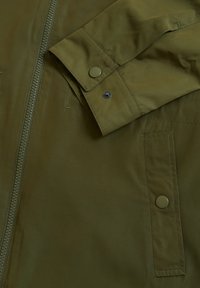 Oliwkowa kurtka o gładkim, matowym wykończeniu. Posiada centralny zamek błyskawiczny, zatrzaski oraz kieszeń w formie naszywki.