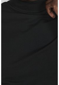 Svart polotröja i mjukt, stretchigt material, med en åtsittande halsringning och slät, jämn textur.