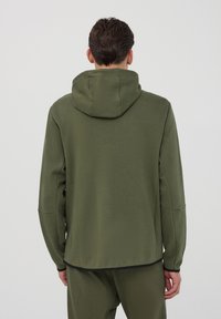 Felpa con cappuccio di colore verde oliva, maniche lunghe, fianchi senza cuciture e orlo diritto. Presenta una texture morbida e un design minimalista.