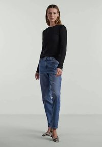 Svart långärmad tröja i avslappnad passform, parat med ljusblå jeans. Accessoarer inkluderar svarta och vita randiga spetsiga skor.