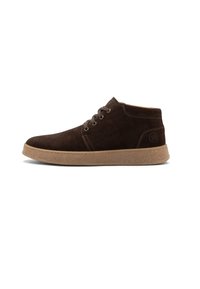 Bottine en suède marron avec un laçage à l'avant, semelle en caoutchouc beige et logo discret sur le talon, présentée en profil latéral sur fond blanc.