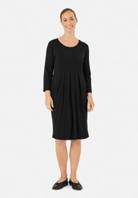 Abito nero al ginocchio con maniche lunghe e scollatura rotonda; presenta pieghe in vita e un tessuto morbido ed elasticizzato.
