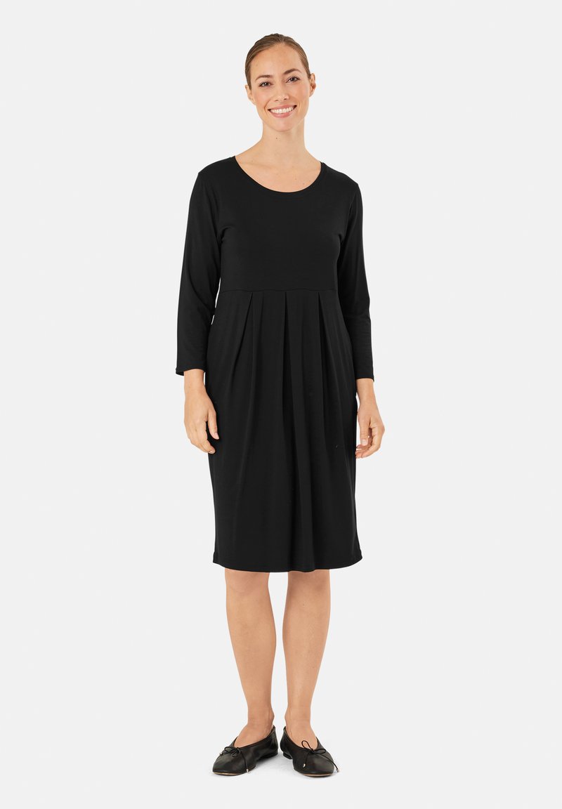 Abito nero al ginocchio con maniche lunghe e scollatura rotonda; presenta pieghe in vita e un tessuto morbido ed elasticizzato.