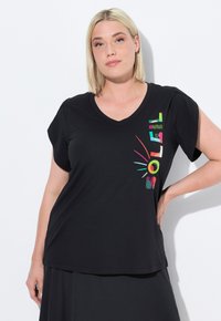Zwarte v-hals t-shirt met korte mouwen, voorzien van kleurrijke grafische tekst en accenten aan de linkerkant, gemaakt van een soepele stof.