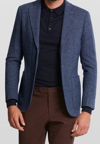 Marinblå herringbone-tygblazer med en skräddarsydd passform, enkelknappsstängning och sidofickor. Matcher med en mörk polotröja under.