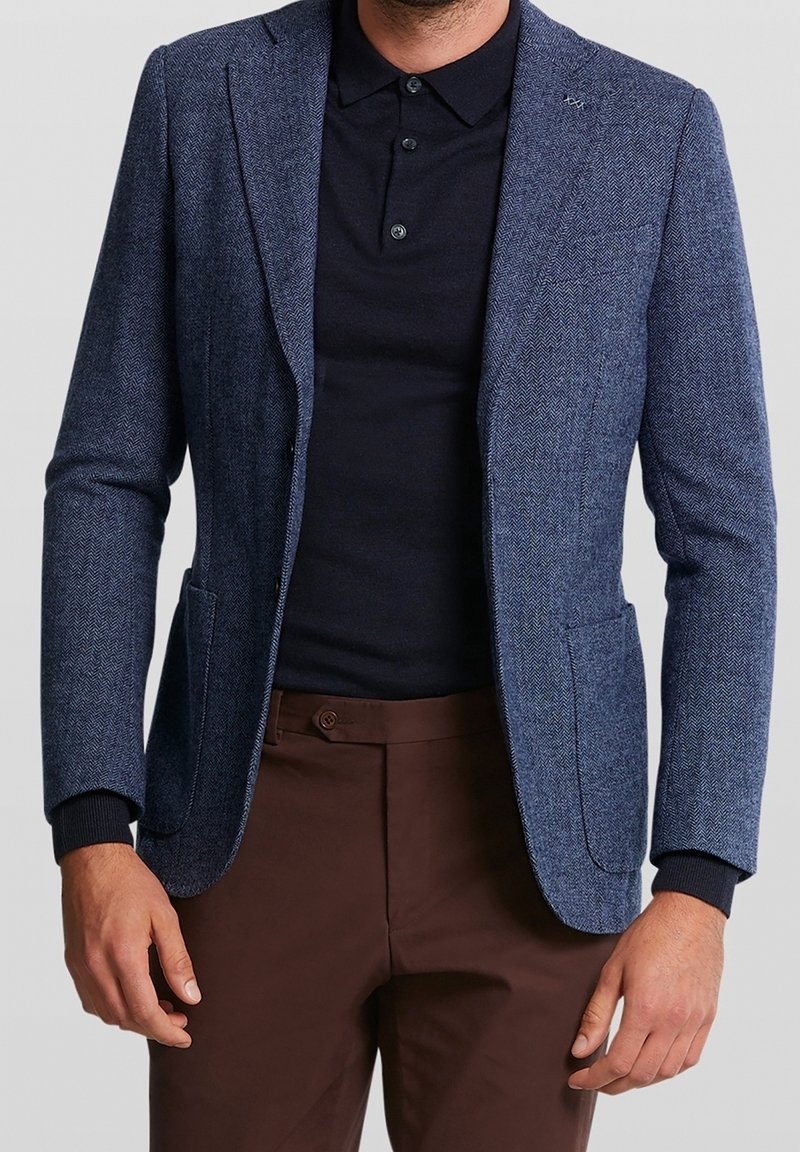 Marinblå herringbone-tygblazer med en skräddarsydd passform, enkelknappsstängning och sidofickor. Matcher med en mörk polotröja under.
