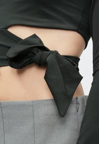 Μαύρο ριχτό τοπ με ραμμένο στοιχείο στο πλάι, συνδυασμένο με μία ανοιχτό γκρι εφαρμοστή φούστα που διαθέτει κλείσιμο με φερμουάρ.