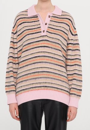 Persoon die een gestreepte gebreide trui met roze kraag en manchetten draagt, gecombineerd met zwarte leren broek, tegen een effen achtergrond.