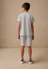 Vaaleanharmaa polo-paitasetti ja shortsit pehmeästä kankaasta, yhdistetty mustavalkoisiin tennareihin. Minimalistinen design, selkeillä linjoilla.