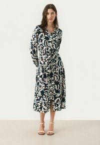 Abito lungo con bottoni in blu navy e crema con un motivo floreale. Presenta maniche lunghe, una vita cinturata e uno spacco sull'orlo.