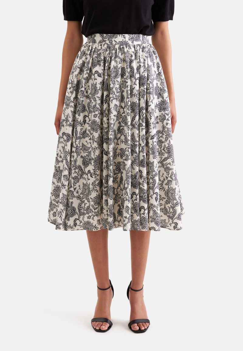 Jupe midi à motif floral noir et blanc, taille froncée, portée avec un top noir à manches courtes et des talons à bride à la cheville noirs.