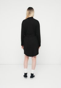 Melna kleita, kas izgatavota no mīkstas auduma, ar garām piedurknēm, jostu vidukļa daļā un nedaudz izliekta apakšmalu. Apvienota ar melniem sneakers un baltām zeķēm.