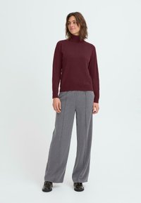 Bordeaux turtleneck trui met lange mouwen, gecombineerd met grijze wijde broekspijpen. De outfit heeft een casual pasvorm en een gladde textuur.