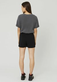 T-shirt gris à manches courtes avec des poignets retroussés, associé à un short noir. Le modèle porte des baskets noires avec des accents rouges.