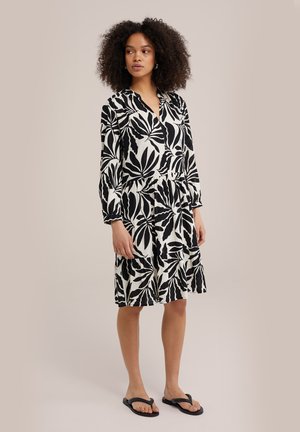 Black and white floral patterned dress with long sleeves, V-neck, tiered hem, and relaxed fit, made from lightweight fabric. Worn with black sandals.