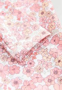 Gėlėmis dekoruota medžiaga su rožinėmis, geltonomis ir žaliosiomis gėlėmis ant balto fono. Lygus paviršius su sulankstytu kraštu.