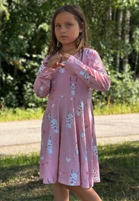 Vaaleanpunainen mekko pitkillä hihoilla, jossa on kani- ja sydänkuvioita. Pehmeä kangas, liehuva hameosa ja pyöreä kaula-aukko.