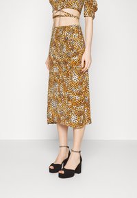 Leopardenmuster-Midi-Rock in Orange, Braun und Creme, aus einem leichten Stoff gefertigt. Kombiniert mit schwarzen High-Heel-Plateausandalen.