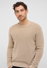 Beżowy sweter dzianinowy o fakturowanej powierzchni, okrągłym dekolcie i długich rękawach. Posiada ściągacze na dole i przy mankietach, co zapewnia dopasowanie.