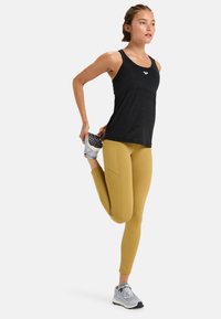 Svart sporttop i en åtsittande design, tillsammans med senapsgula leggings med en mjuk textur. Grå sneakers med snörning.