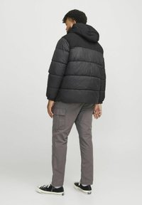 Geacă puffer neagră cu glugă, având un design matlasat și manșete elastice, asociată cu pantaloni cargo gri și adidași negri.