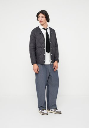 Quiltet sort jakke med trykknapper, hvid skjorte, sort slips og løse blå denimbukser. Afsluttet med grå og hvide sneakers.