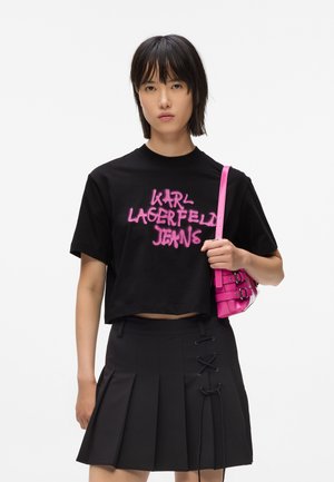 Mustat lyhythihaiset t-paidat, joissa on vaaleanpunaisella spraymaalilla kirjoitettu "KARL LAGERFELD JEANS" -teksti. Musta kireä hame, jossa on nauhakiinnityksellä yksityiskohtia, ja pieni vaaleanpunainen käsilaukku.