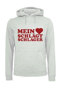 Ljusgrå hoodie med en framficka, med röd text och ett hjärtsymbol som säger "MEIN ♥ SCHLÄGT SCHLAGER." Enkelt design och avslappnad passform.