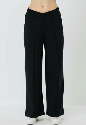 Schwarze weit geschnittene Hose mit einem strukturierten, gerafften Bund. Aus einem glatten Stoff gefertigt, mit vorderen Falten und einem fließenden Fall.