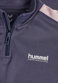 Dunkelblaues Trainingsoberteil mit halbem Reißverschlusskragen, hellrosa Akzent an der Schulter und weißem "hummel PERFORMANCE" Logo auf der Brust. Angenehme Textur.