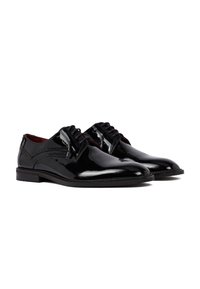 Een paar glanzende zwarte leren dress shoes met veters en brogue-details op een witte achtergrond.