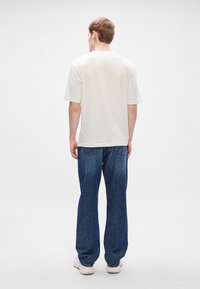 Tricou alb din bumbac, cu mâneci scurte, asociat cu blugi lejera din denim albastru. Blugii au un design clasic cu cinci buzunare și cusături vizibile.