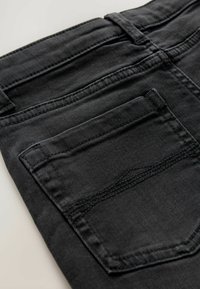 Jean en denim noir avec une poche arrière, au design droit et avec des surpiqûres contrastantes. Le tissu a une texture lisse.