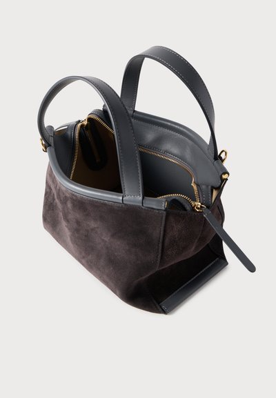 Τσάντα χειρός από σκούρο γκρι σουέτ με δερμάτινες λεπτομέρειες, διπλές λαβές και εσωτερικά διαμερίσματα, περιλαμβάνοντας μία θήκη με φερμουάρ και χρυσές μεταλλικές λεπτομέρειες.