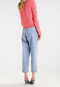 Maglione lavorato a maglia rosso con trama, jeans azzurri a vita alta con risvolti, scarpe con tacco grigie. Vista posteriore che mostra il design dell'outfit.
