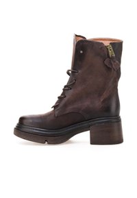 Brune læder ankelstøvle med rund tå, snørebånd foran, sidelukning med lynlås og en kraftig træhæl. Teksturopbygning og slidte detaljer.