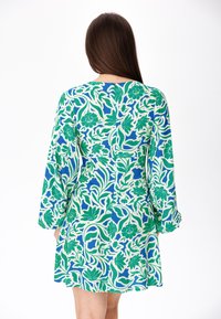 Vestido floral con base azul y patrones florales en verde y crema, manga larga y abertura en la parte posterior. Textura de tela suave.